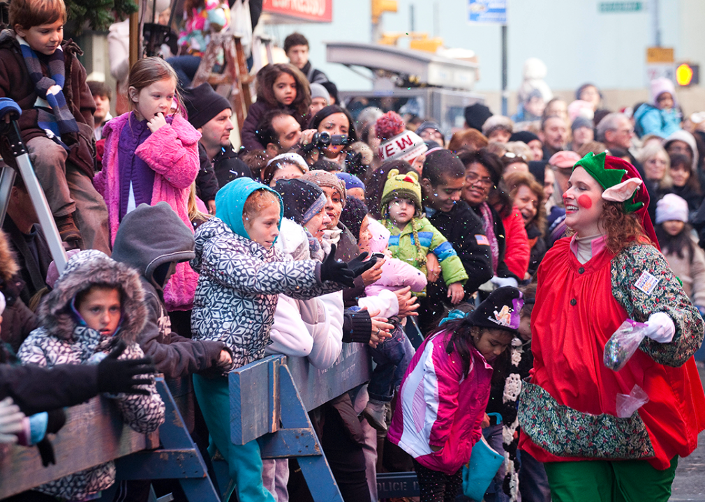 A woman dressed in an elf costume sprinkles young spectators with confetti.