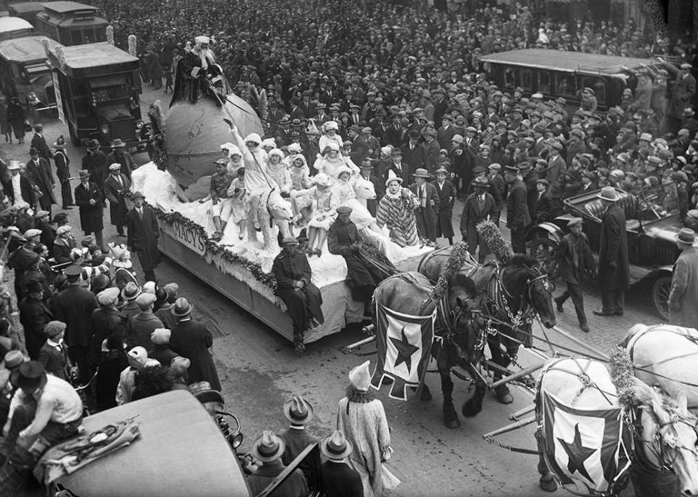 Crowds on Broadway watch a parade float with Santa Claus seated atop a large globe being led by polar bears statues.