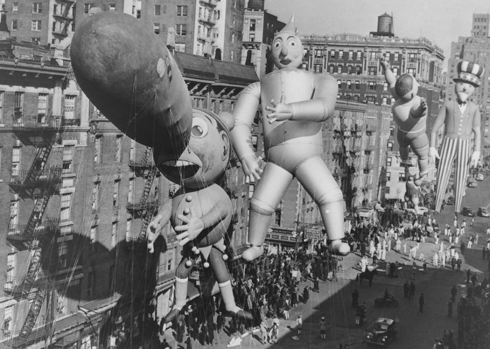 Pinocchio, The Tin Man, and Uncle Sam balloons photographed from an office building. The balloons reach above the the seven-storey building they are passing.